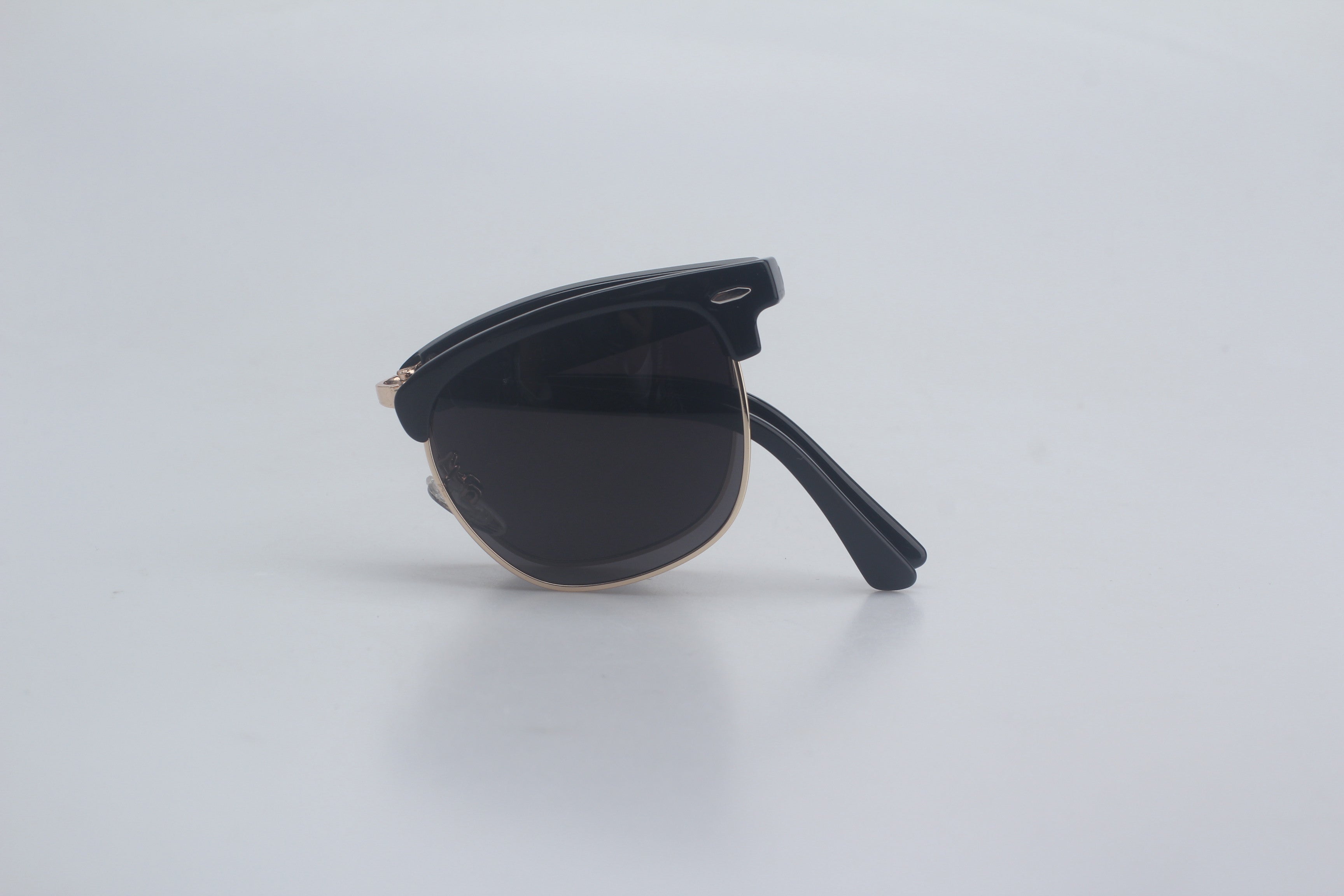 Elegant black Clubmaster sunglasses with glossy TR90 upper frames, rose gold-tone metal lower rims for a semi-rimless look, deep smoke polarized lenses offering anti-reflective clarity, displayed folded on simple white platform for versatile unisex eyewear range, chic designer sun specs, maximum UV filtering glasses, retro-modern hybrid shades, premium optic style companions, active lifestyle eye shield accessories.