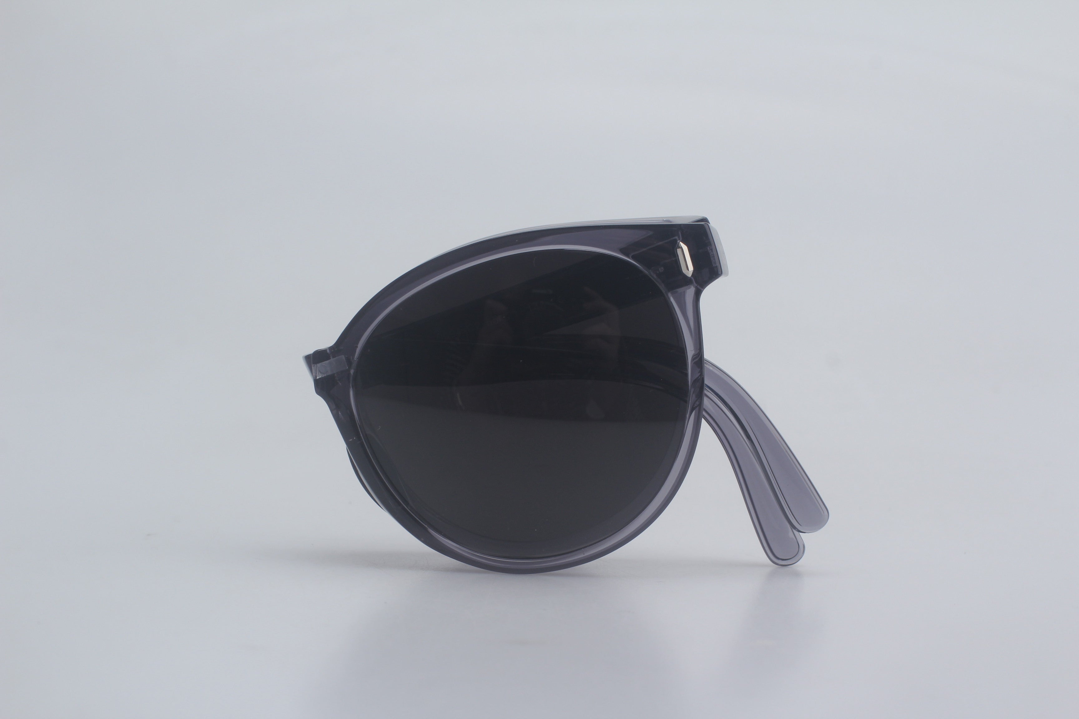Translucent smoke gray oval sunglasses with dark lenses and slim transparent temples, presented folded on clean white backdrop for modern unisex eyewear selection, trendy designer sunshades, UV shielding spectacles, classic yet contemporary sunnies, elite vision protection accessories.